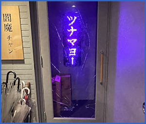 入口に「ツナマヨ」の文字のパープルライトがある割れたガラス画像